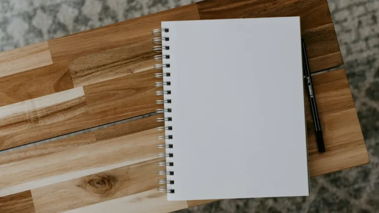 Blank spiral notebook on a wooden desk beside a black pen