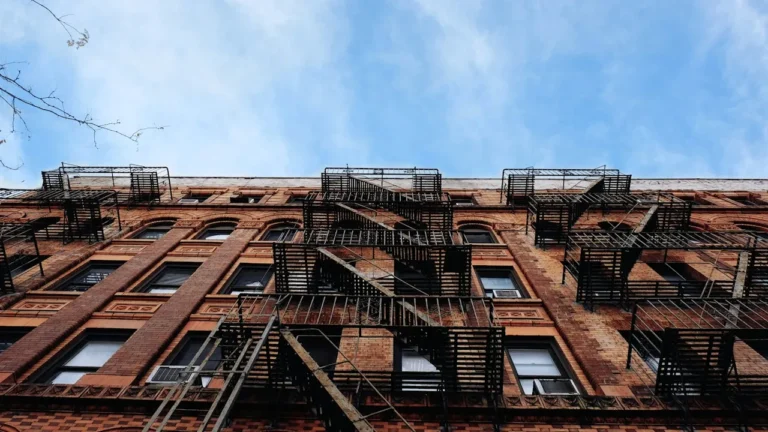 Brick apartment building with exterior fire escapes beneath a blue sky