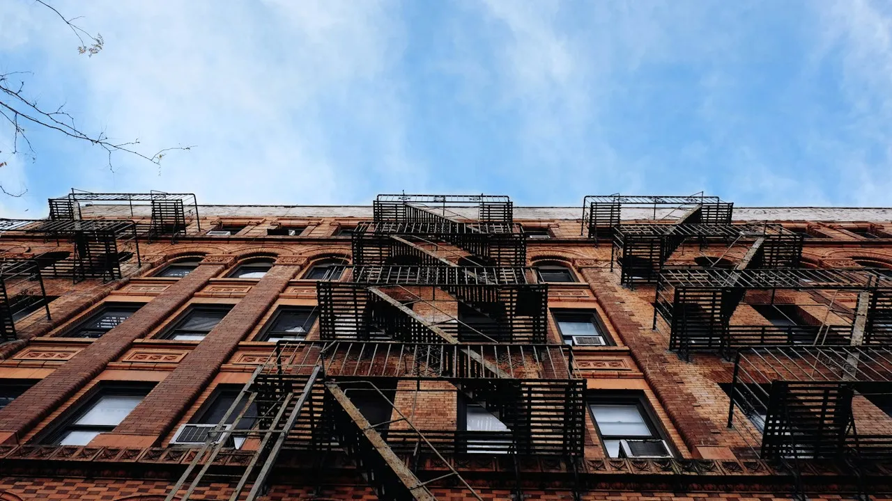 Brick apartment building with exterior fire escapes beneath a blue sky